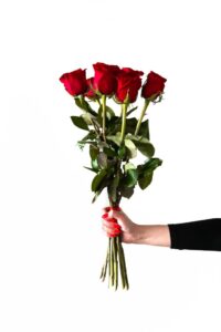 A hand with red-painted nails holding a bouquet of red roses against a white background, symbolizing love and romance.