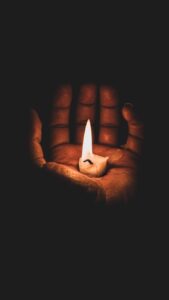 A dark-skinned hand cupping a small, flickering candle in total darkness, symbolizing resilience and creativity during power outages. 